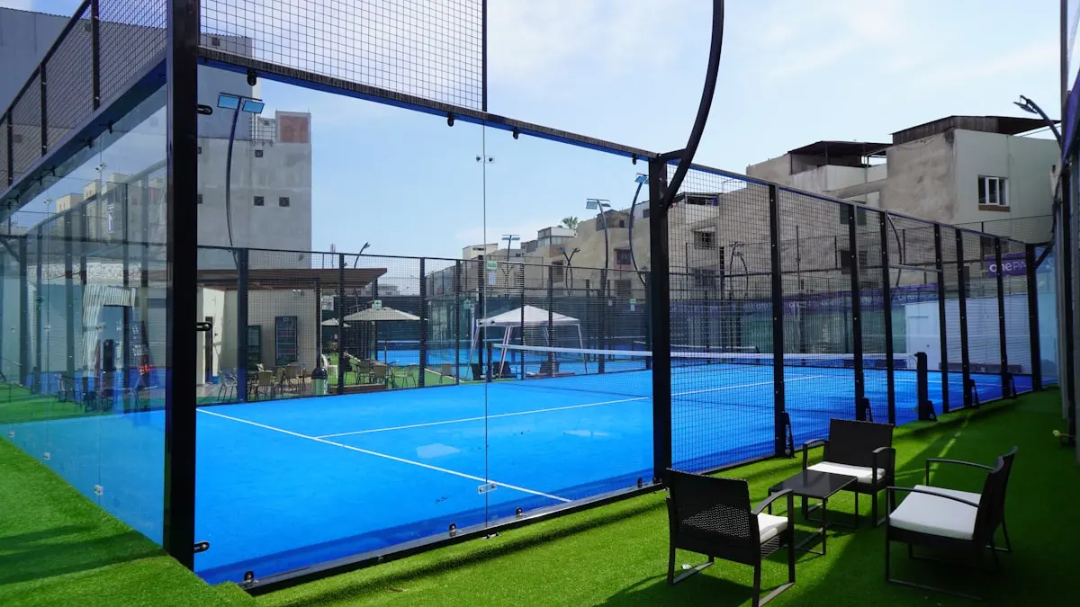 Courtside seating on green turf beside a glass padel court